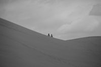 two people standing on top of a sand dune