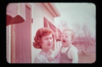 a woman holding a baby in front of a house
