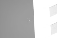 a black and white photo of a plane flying over a building