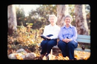two women sitting on a bench in a park